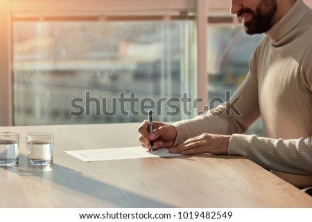Berded man signing contract at office desk. Side view caucasian man with pen in his hands.
