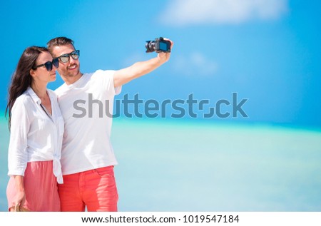 Selfie couple taking pictures on the beach. Tourists people taking travel photos on their holidays.
