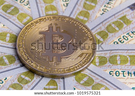 Old coin golden bitcoin on the background of hundred-dollar bills spread out in a circle.