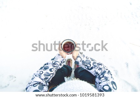 Cup of tea holding in woman hand. Winter background. Hot drink with foam. Snow and cold weather. Coffee break. Concept of drink in a nature