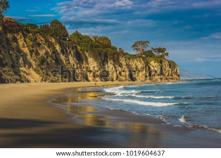 Beachside view of beautiful blue Pacific Ocean and stunning cliffs surrounding Dume Cove on a sunny day with clouds in the sky, Point Dume, Malibu, California Royalty-Free Stock Photo #1019604637