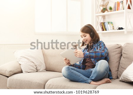 Little girl watching cartoon on digital tablet. Gadgets and technology concept, playing online game while sitting on couch in living room at home, copy space