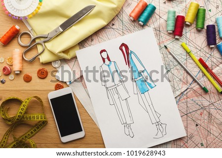 Creating new fashion collection background. Hand drawn sketches of clothes, smartphone, color swatches and threads on wooden table, top view. Creativity, dressmaking and design concept