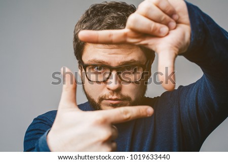 Young business man in glasses focusing with fingers, framing with hands isolated on grey background. Close up portrait