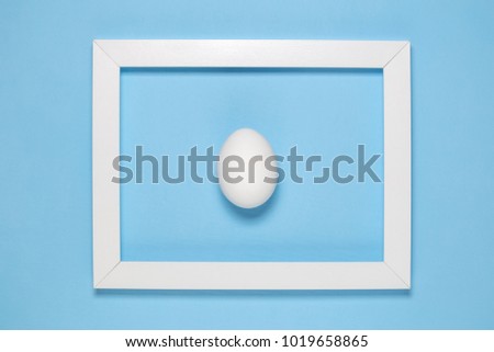 Flat lay of white egg in wooden frame on blue background minimal concept.
