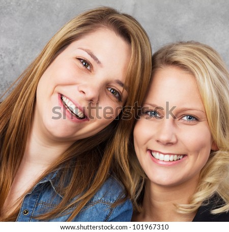 Portrait of two cheerfully smiling young teenage women looking at the camera. Studio shot against a gray background.