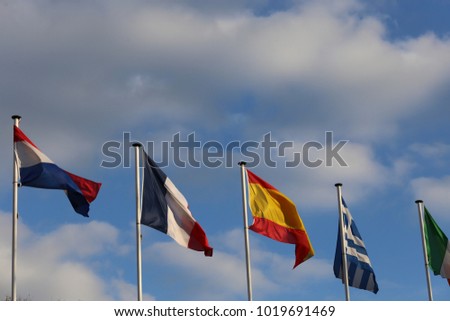 Close up view of a row of colorful flags fluttering in the blue sky. Many countries represented. White vertical thin poles. Symbol of the international community. Many flags waving in the wind.  