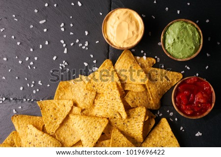 Mexican nachos with sauces tomato ketchup, cheese and guacamole in wooden bowl on dark background, top view, copy space. Delicious salty corn chips triangular nachos snack for party Royalty-Free Stock Photo #1019696422