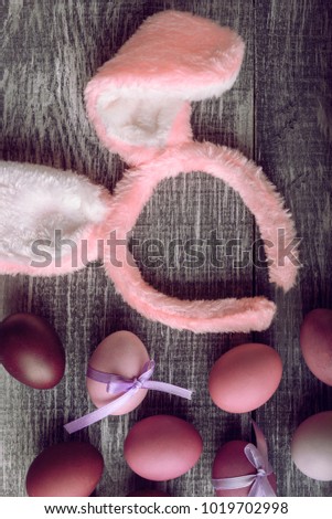 Easter eggs in a fashionable coloring on a gray wooden background with a female hoop with Easter bunny ears