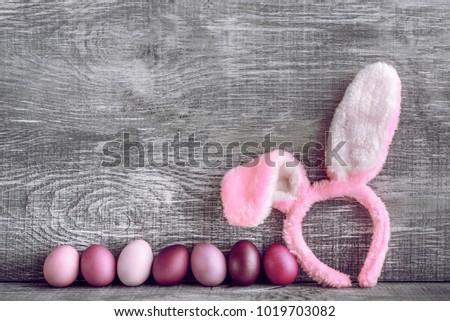 Easter eggs in a fashionable coloring on a gray wooden background with a female hoop with Easter bunny ears