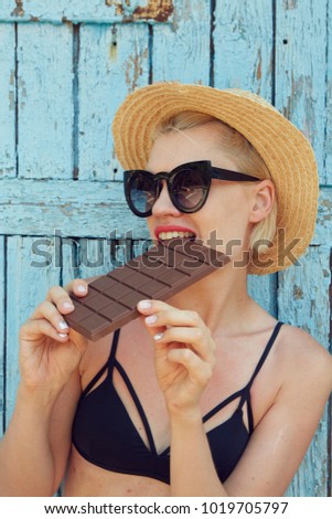 Young attractive woman in sunglasses and in straw hat eating chocolate on a blue background. Film efect