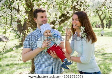 young happy family walking outdoor. Parents hold child on hands and rejoice. They are happy together. Smile each other
