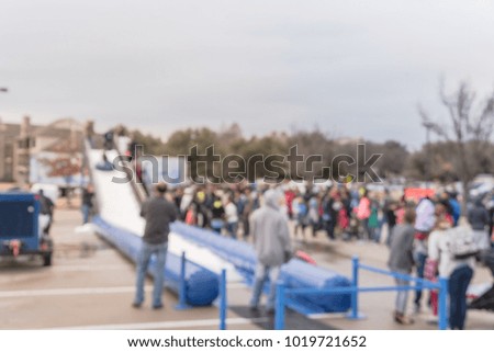 Blurred child sliding on giant inflatable snow tube at wintertime community event in Texas, USA. People talking picture, large group of diverse multiethnic crowd family members waiting.