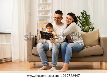 family, technology, parenthood and people concept - happy mother and father showing tablet pc computer to baby daughter at home Royalty-Free Stock Photo #1019722447