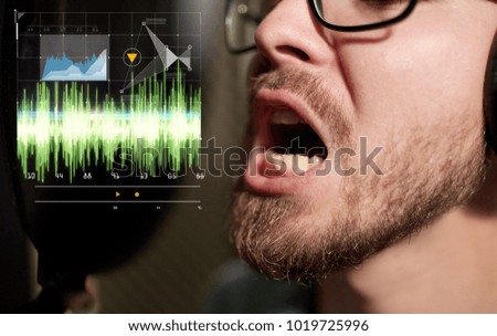 music, show business, people and technology concept - male singer with headphones and microphone singing song at sound recording studio