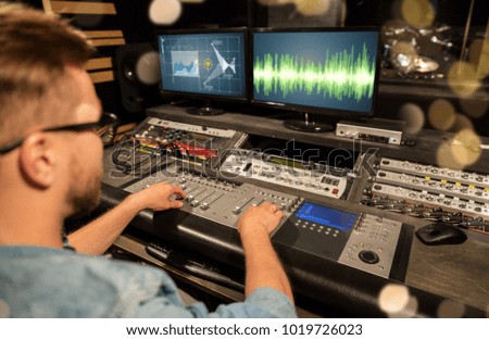 music, technology, people and equipment concept - man at mixing console in sound recording studio over festive lights