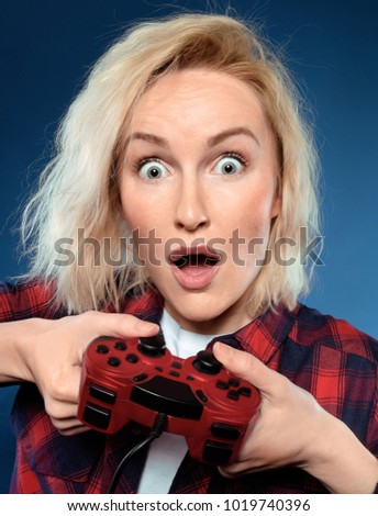 Young funny blonde woman gamer is playing a video game with red joystick and she is the happy winner. She is excited to play with her game console, 
girl with game pad is yelling with joy