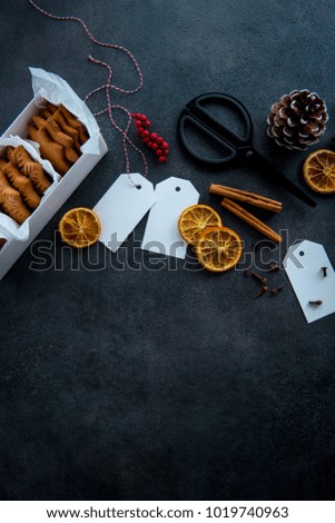 Gift wrapping of Christmas cookies. Top view of table with gingerbread cookies in paper box, dried orange slices, cinnamon sticks, scissors, tags, pinecone and holly berry. Flat lay.