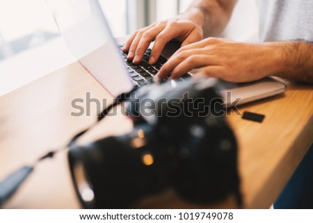Close frame of male hands working on a laptop next to a professional camera.