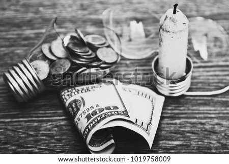 Black-and-white photo of scattered coins of light bulb fragments and dollars on the table