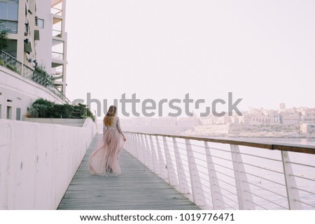 Carefree woman in elegant dress enjoying city morning views in warm day. Outdoor photo of cute female girl in European town. Embankment