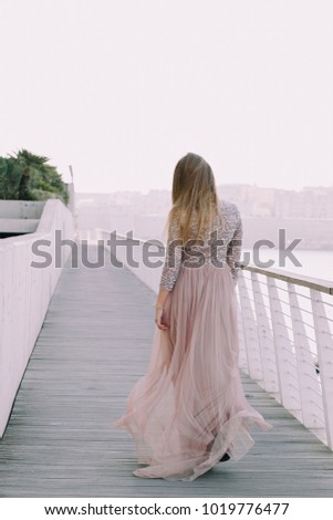 Carefree woman in elegant dress enjoying city morning views in warm day. Outdoor photo of cute female girl in European town. Embankment