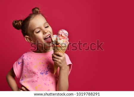 Pretty baby girl kid eating licking big ice cream in waffles cone with raspberry happy laughing on red background
