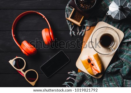 Wooden black table with blank screen smart phone,headphone,sunglasses and cup of coffee.View from above.