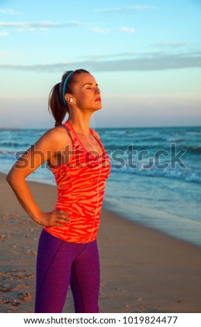 Refreshing wild sea side workout. relaxed fit woman in sports gear on the seashore at sunset with headphones listening to the music