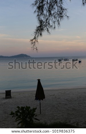 Seascape view of the principal beach of besar one of the two islands of Pulau Perhentian in Malaysia. Calm sea with boats. Mountain silhouettes. Sunset with purple sky. Picture taken on 24th July 2015