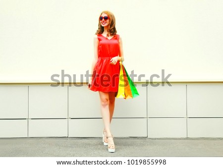 Fashion pretty smiling woman in red dress with a shopping bags in the city