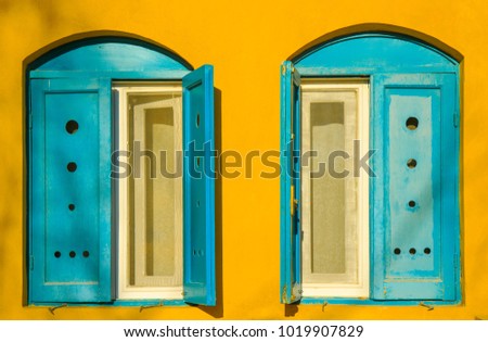 Blue old style wooden windows, symmetry in open doors, yellow house wall background in small town, minimal style of simplicity, trendy look, contrast bright colors, modern postcard art design concept