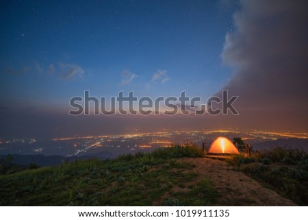 Illuminated orange camping tent on the hill with city light background