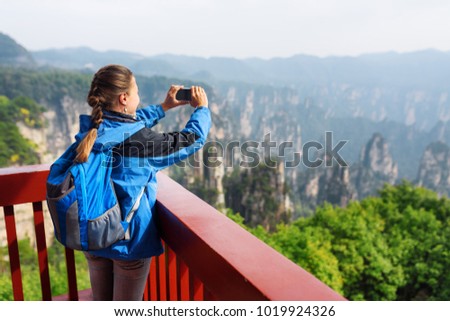 Young female tourist with smartphone taking photo and enjoying mountain view in the Zhangjiajie National Forest Park, Hunan Province, China. Her hair braided in French plait. Outdoor portrait.