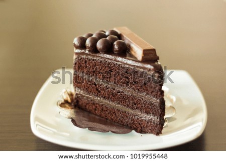 Closeup slice piece of dark chocolate cake on white plate decorated with chocolate round.