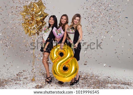 Three beautiful girls in black dresses are holding tulip bouquets. Eight-shaped big balloon. Confetti. Happy woman's day  