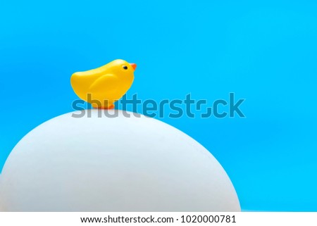 Little toy yellow chick sits on a big egg on a blue background