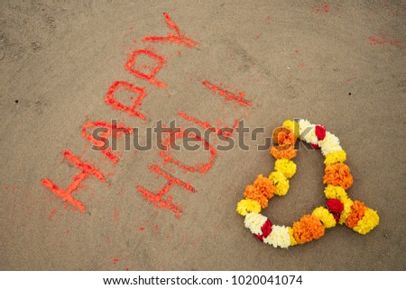 the inscription on the sand Happy Holi orange dust and a flower garland in the form of a heart
