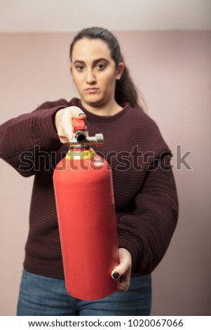 Young woman pointing a red fire extinguisher forwards towards the camera with a serious expression and focus to the canister
