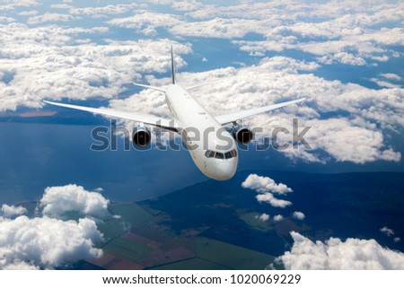 White aircraft in flight. The passenger plane flies high above the clouds and earth. Front view of airplane.