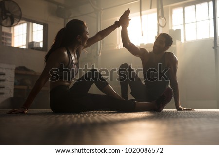 Healthy man and woman sitting on floor and giving each other high five at the gym. Fitness people after successful exercising session in gym. Royalty-Free Stock Photo #1020086572