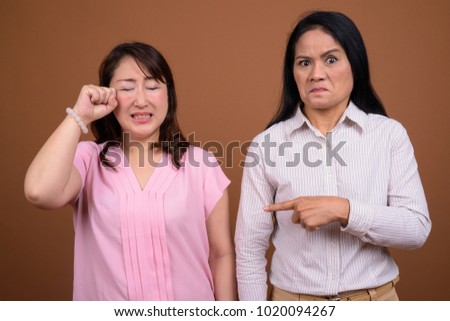 Studio shot of two mature Asian businesswomen together against brown background