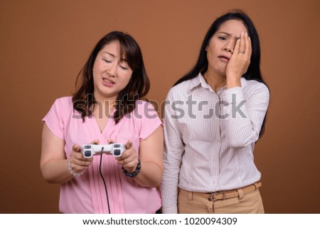 Studio shot of two mature Asian businesswomen together against brown background