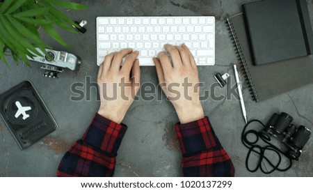 Dark table with man's hands typing. Creative layout  with copy space top view. Travel accessories: passport, camera, binoculars, notebook, laptop keyboard. Next adventure booking and planing.
