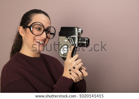 Nerdy young woman in large over sized glasses laughing and holding a 8mm film camera pointed towards blank copy space