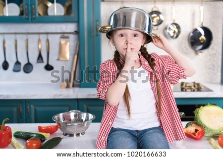 cute child with pan on head looking at camera and gesturing for silence