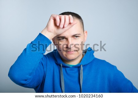 portrait of a man tired and wiping brow from his forehead, wearing a blue hoodie, isolated on a gray background