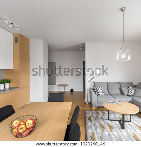 Square photo of modern open space dining room with table and gray sofa