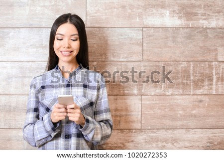 Beautiful young woman with mobile phone near wooden wall