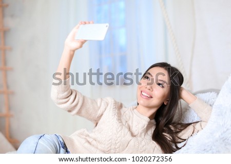 Beautiful young woman taking selfie with mobile phone at home